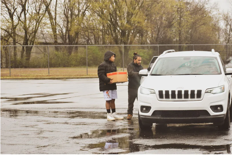 2 men carrying food to a car.