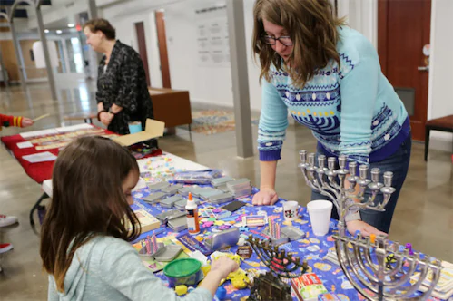 Lady helping a small girl with crafts to celebrate Hanukkah